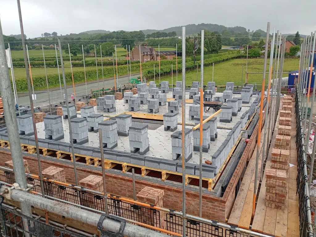 Upper floor deck with blocks loaded out, the facing brick outer leaf round the edge and fields and hills behind
