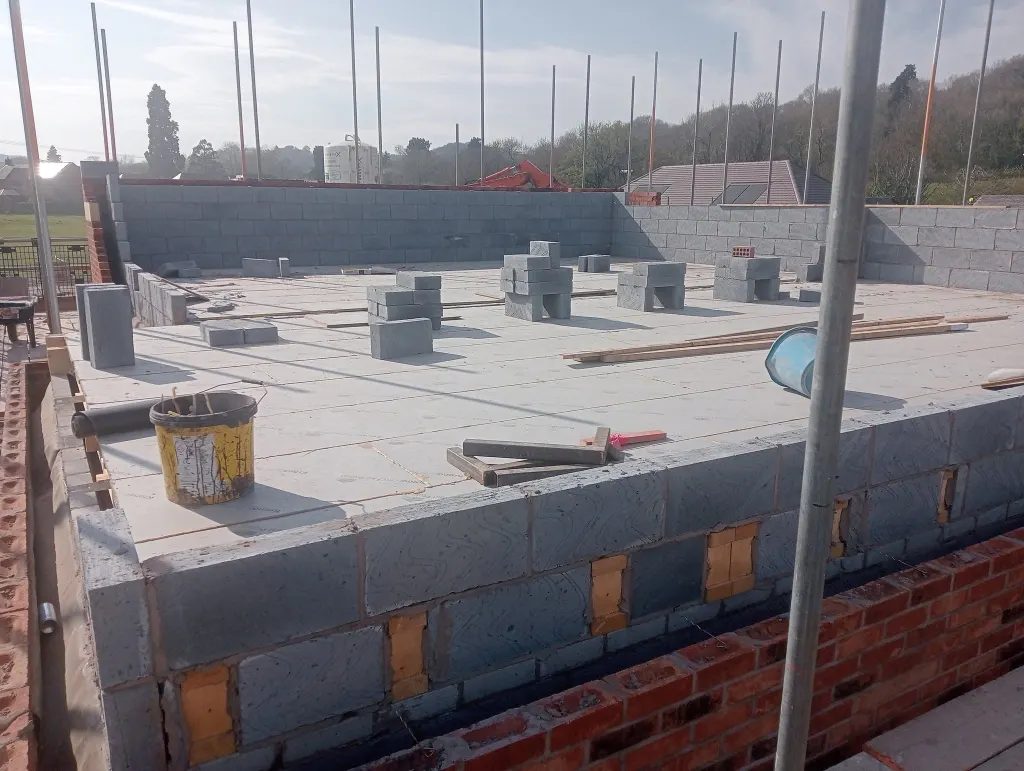 Blockwork inner leaf rising on a first-floor deck, with blocks, timber and a mortar tub on the floor and brick below