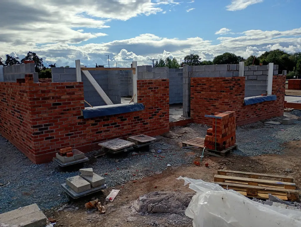 Red facing brick outer leaf with grey blockwork inner leaf on a bungalow plot, brick piles and packs around the walls