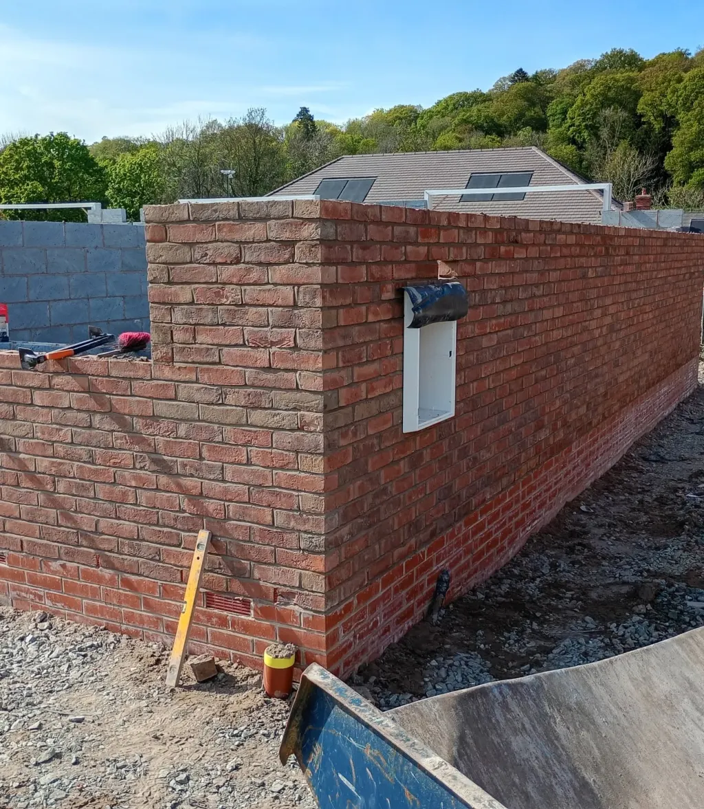 Crisp corner in multi red facing brick with a meter box and cloaked head, a spirit level and tools left on the wall