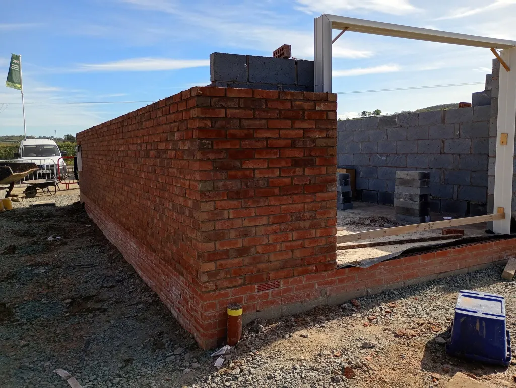Return of red facing brick with blockwork inner leaf behind and a door frame propped, cavity trays visible at base