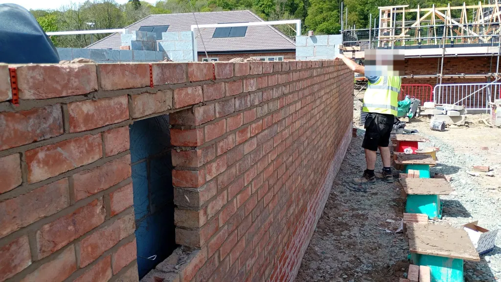 Close view of new facing brick with red wall ties in the bed joint and an opening, a bricklayer checking the wall
