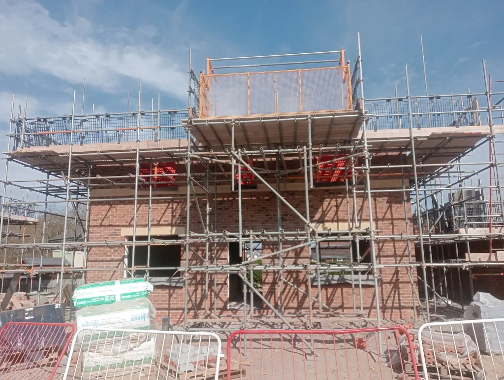 Brick house behind full scaffold with a loading bay on top, mortar and sand bags stacked in front of the barriers