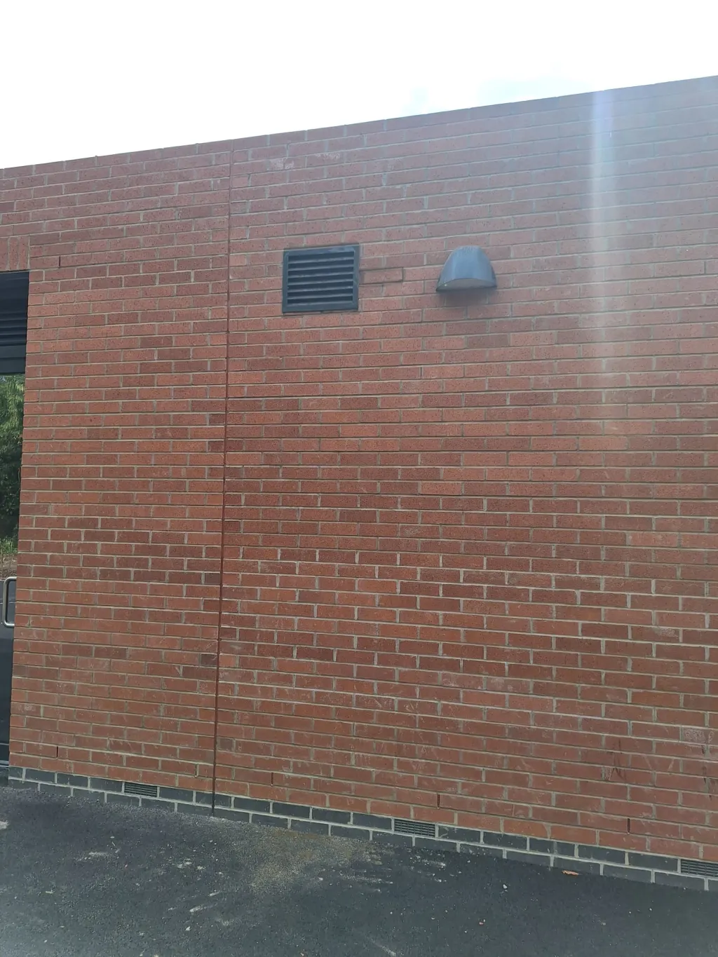 Plain gable wall in red facing brick with a dark brick base course, a louvre vent and a round extract hood near the top