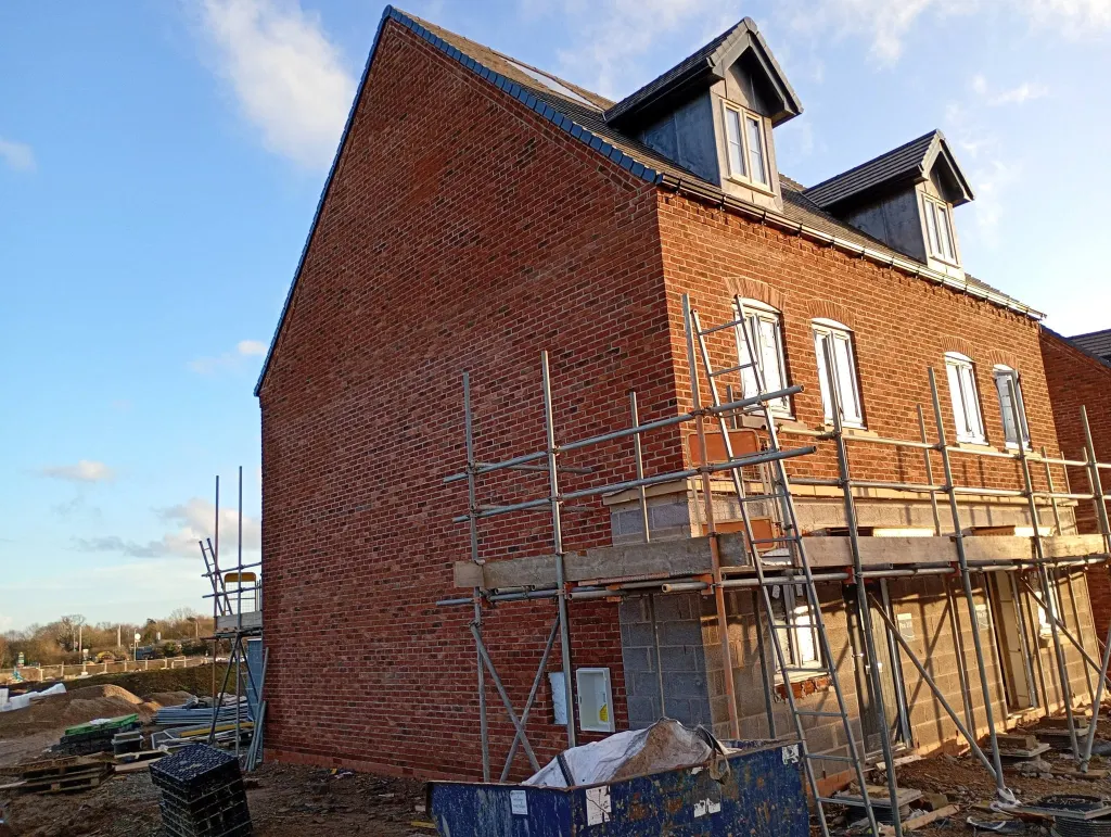 Three-storey townhouse in red facing brick with two roof dormers and a tall gable, scaffold still up at ground floor