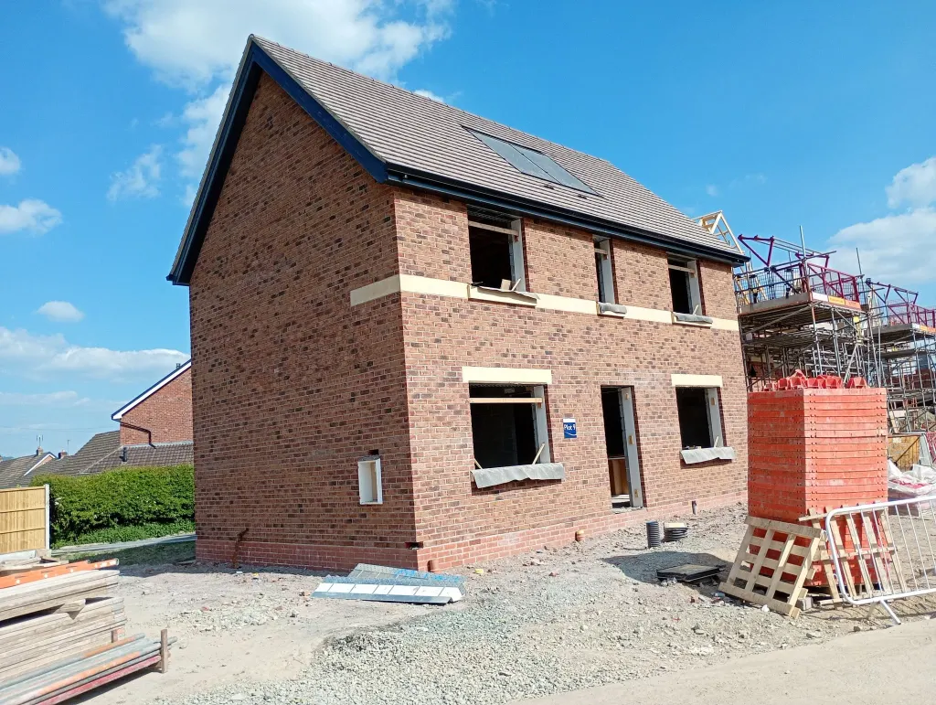 Gable end and front of a two-storey brick house with buff stone sills and banding, pallets and a brick pack beside it