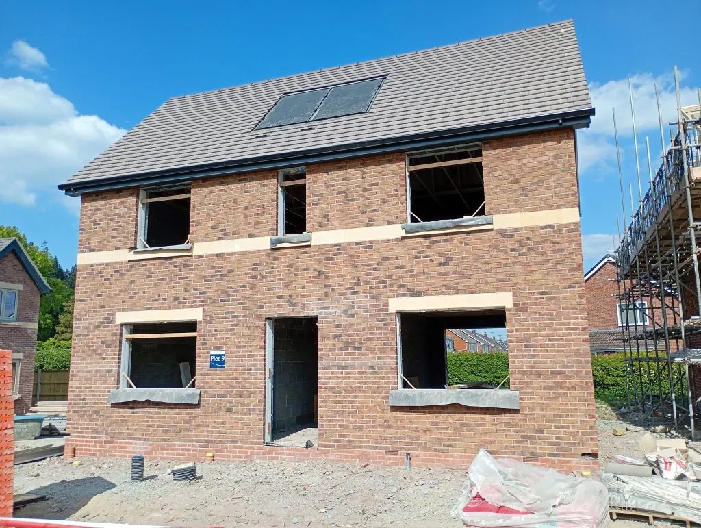 Two-storey house in multi red facing brick with a buff stone band and heads, roof on and window openings still empty